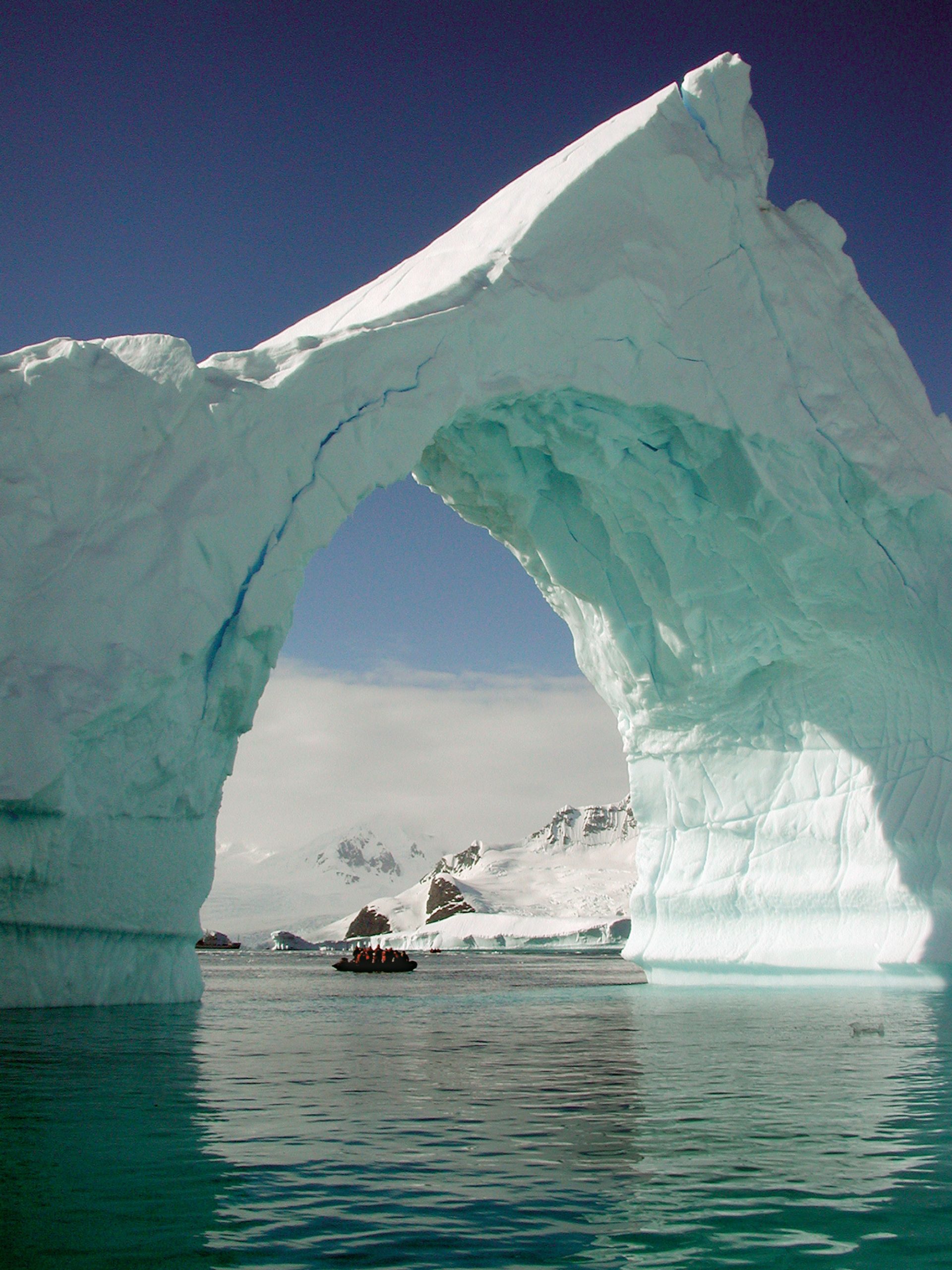 A zodiak carries a group of WHOI Associates and other ecotourists through an iceberg arch off Antarctica.