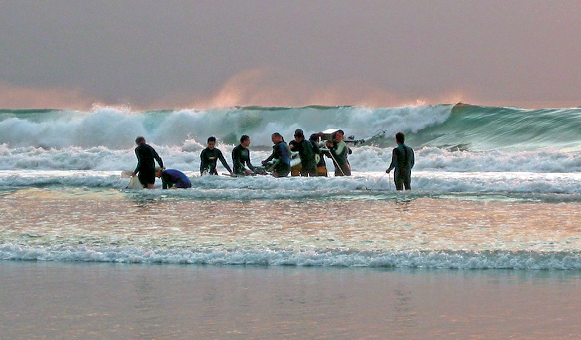 Researchers carrying an instrument tower into the surf